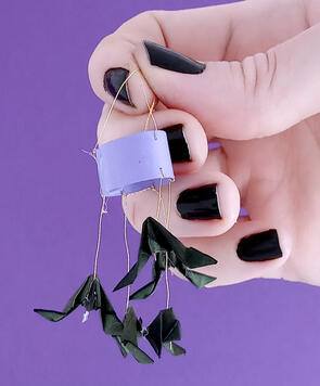 Tiny paper mobile of bats held by hand with black painted nails.